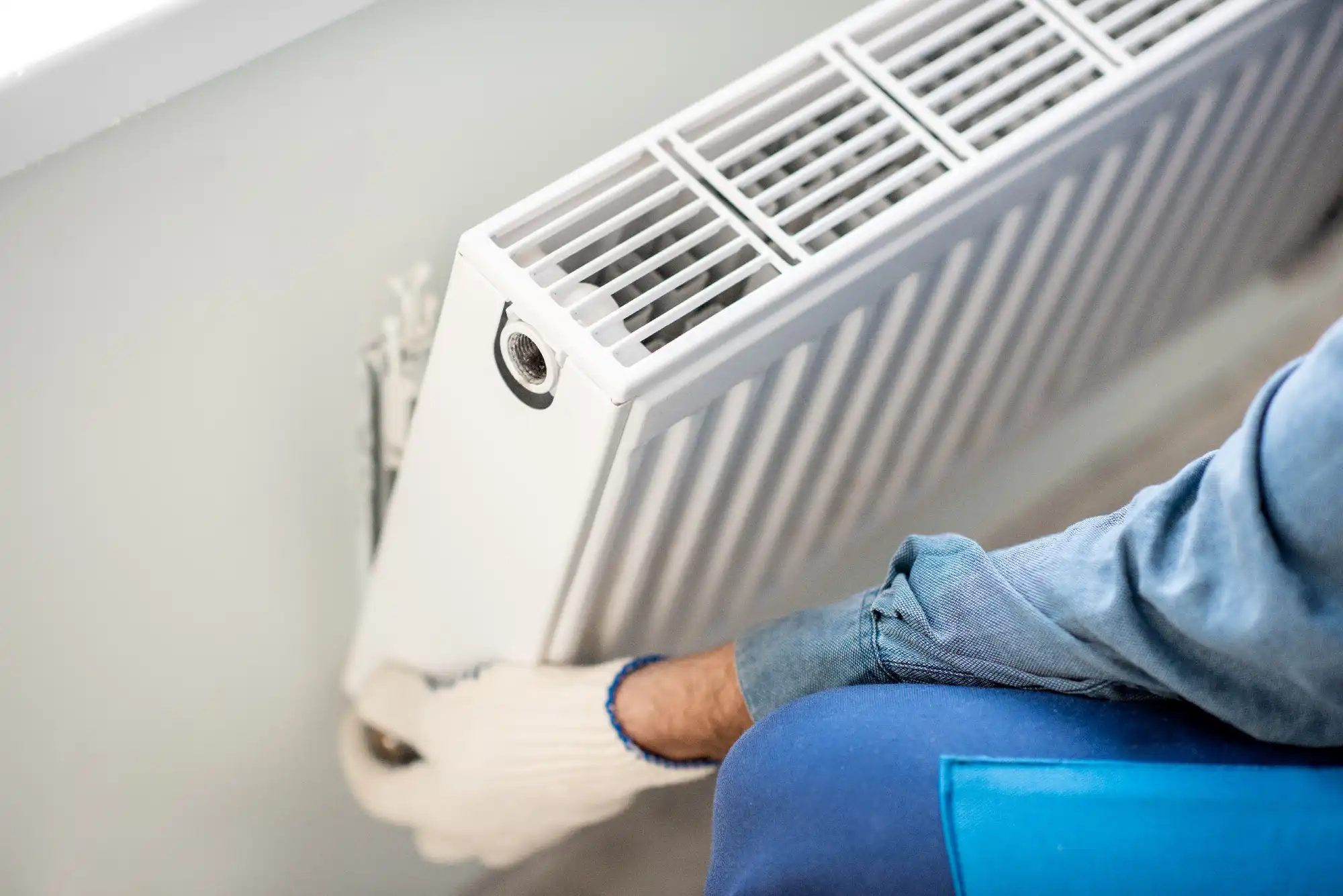 A person sitting on a blue chair next to a heater.
