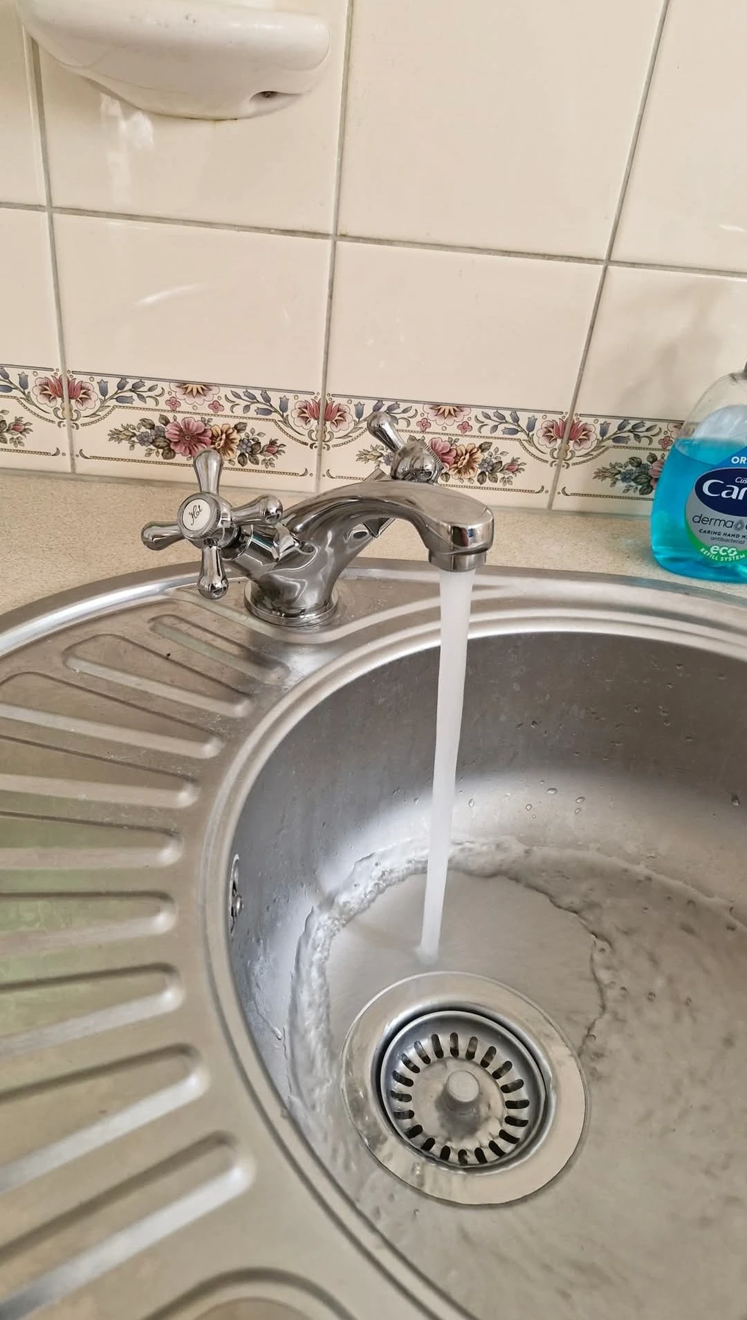 Round chrome kitchen sink with running tap.